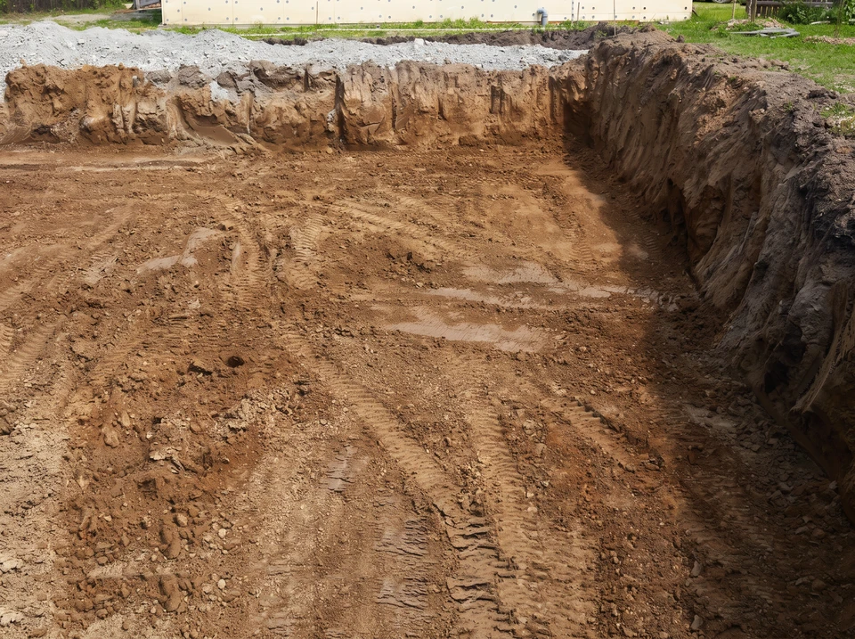 Talus en pente stabilisé avec enrochement de blocs de pierre calcaire empilés régulièrement, formant une protection massive contre l'érosion. Le terrain en arrière-plan montre une excavation d'aménagement. Végétation méditerranéenne environnante, ciel dégagé. Zone de chantier clairement délimitée avec engins de terrassement visibles en arrière-plan.