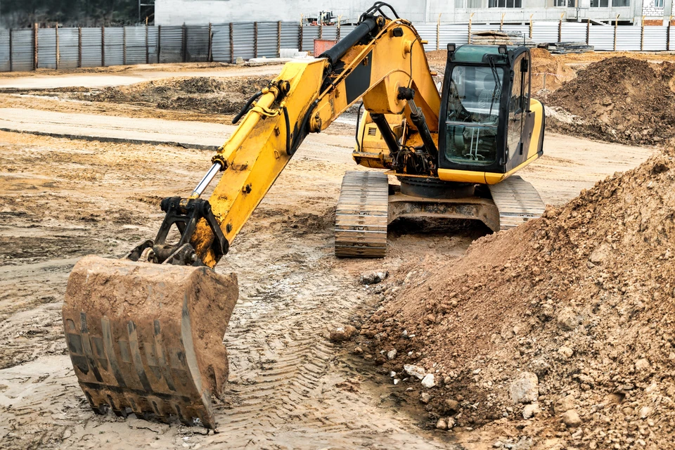 Pelle hydraulique sur chenilles en action sur un chantier de démolition, godet de démolition renforcé équipé de dents hydrauliques broyant des éléments de béton et de gravats, cabine de l'opérateur visible, terrain urbain ou périurbain en arrière-plan, travaux publics.